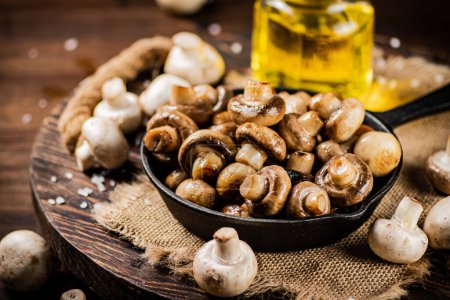 Téléchargez les photos : Frying pan with fried mushrooms on a wooden tray. On a wooden background. High quality photo - en image libre de droit