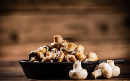 Téléchargez les photos : A frying pan with fried mushrooms on the table. On a wooden background. High quality photo - en image libre de droit