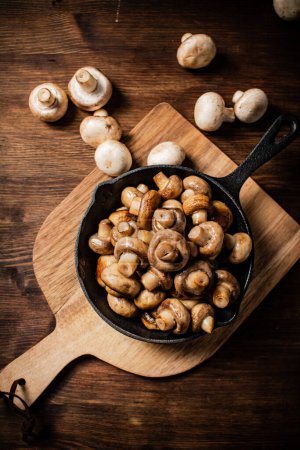 Photo for Fried mushrooms in a frying pan on a cutting board. On a wooden background. High quality photo - Royalty Free Image