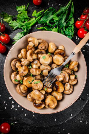 Téléchargez les photos : Fried mushrooms in a bowl with greens and tomatoes on a stone board. On a black background. High quality photo - en image libre de droit