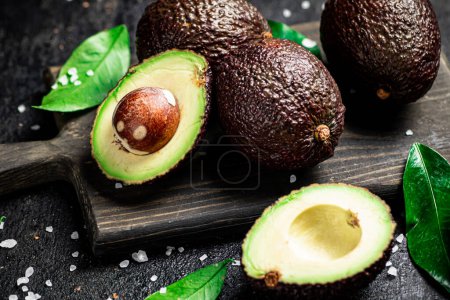 Photo for Cut avocado with leaves on a cutting board. On a black background. High quality photo - Royalty Free Image