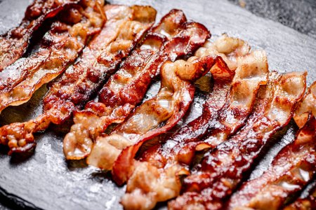 Téléchargez les photos : Bandes de bacon frit sur fond noir. Photo de haute qualité - en image libre de droit