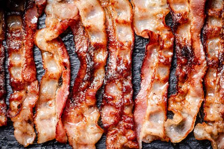 Téléchargez les photos : Bandes de bacon frit sur fond noir. Photo de haute qualité - en image libre de droit