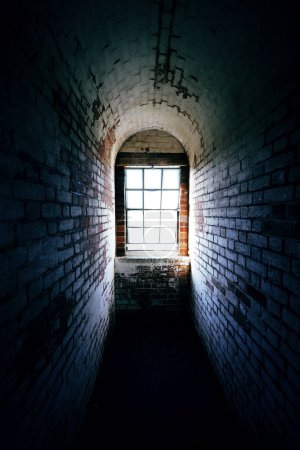 Photo for Spooky narrow old brick corridor with light shining through a window at the end - Royalty Free Image