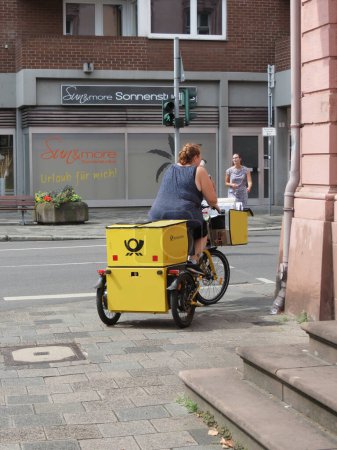 Téléchargez les photos : WORMS, GERMANY - CIRCA AUGUST 2022: Postwoman delivering mail by bike - en image libre de droit