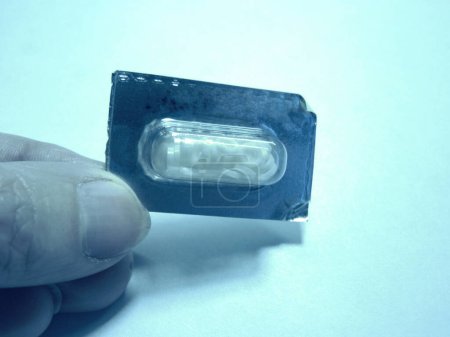 main tenant la pilule de contraste pour l'étude de l'image du tube digestif dans sa plaquette thermoformée, dans les tons bleu clair et sépia