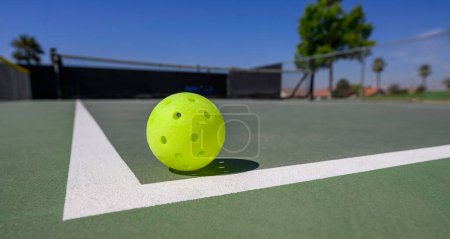 Tight focus on a pickleball on a court with white lines. The sport of pickleball has become the fastest growing sport in America.