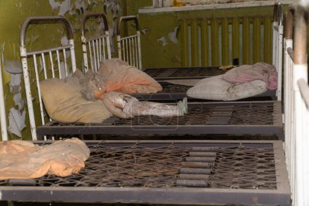 Foto de Una muñeca vieja sobre una cama oxidada con almohadas viejas dentro de un jardín infantil abandonado en la zona de exclusión de desastres nucleares de Chernobyl - Imagen libre de derechos