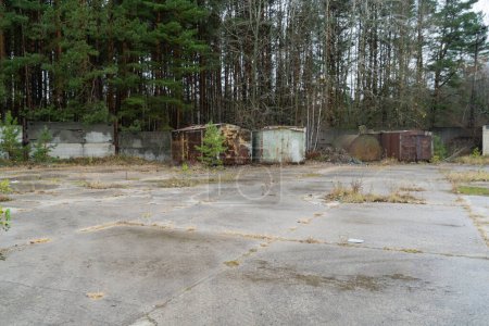 Foto de Contenedores abandonados viejos y oxidados en un aparcamiento con fondo de bosque autum en la zona de exlusión radiactiva de Chernobyl - Imagen libre de derechos