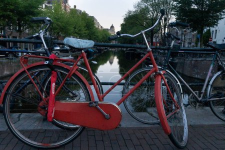 Foto de Bicicleta vintage roja acostada en una valla metálica con otra bicicleta con amstel river al fondo - Imagen libre de derechos