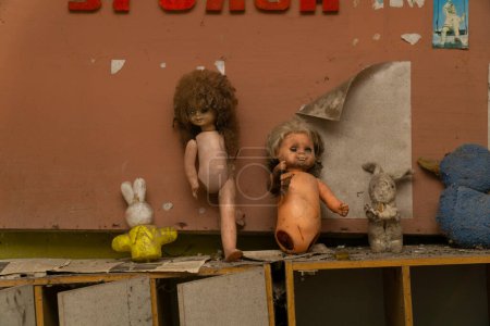 Foto de Dos muñecas viejas y dos conejos viejos juguetes sobre un mueble de madera dentro de un jardín infantil abandonado en la zona de exclusión radiactiva de Chernobyl - Imagen libre de derechos