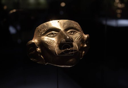 Foto de Cerca de un antiguo rostro de máscara de oro indígena con forma antropomórfica en el museo dorado - Imagen libre de derechos