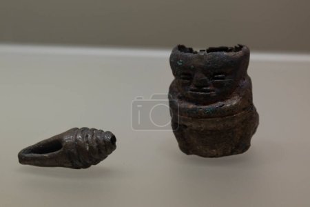 Téléchargez les photos : Gros plan sur une ancienne petite figure anthropomorphe indigène de cuivre près d'une coquille de cuivre au musée colombien d'or - en image libre de droit