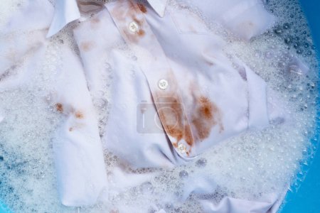 Photo for Dirty choclate stain on white shirt soaking in water with detergent water dissolution, washing cloth - Royalty Free Image