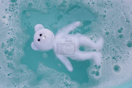 Téléchargez les photos : Faire tremper la poupée d'ours en peluche dans un détergent à lessive avant de la laver. Concept blanchisserie, Vue dessus - en image libre de droit
