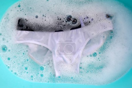 Téléchargez les photos : Sous-vêtements pour hommes trempés dans de l'eau détergent dissous avec bulle de mousse blanche. Concept de blanchisserie - en image libre de droit