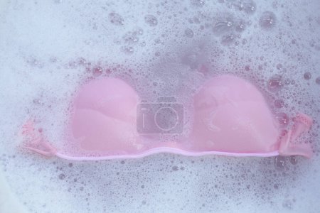 Lady bra soaked in water dissolved detergent with white foam bubble. Laundry concept