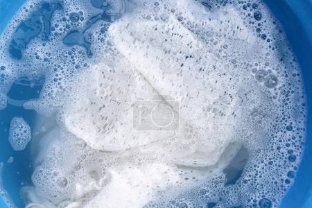 Téléchargez les photos : Robe en dentelle pour femme imbibée d'eau détergente dissoute avec bulle de mousse blanche. Concept de blanchisserie - en image libre de droit