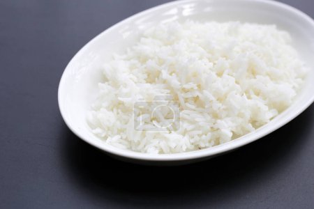 Gekochter Reis in weißem Teller auf dunklem Hintergrund.