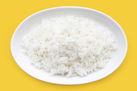 Gekochter Reis in weißem Teller auf gelbem Hintergrund.