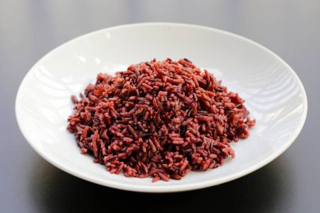 Cooked black berry rice in white plate on dark background.