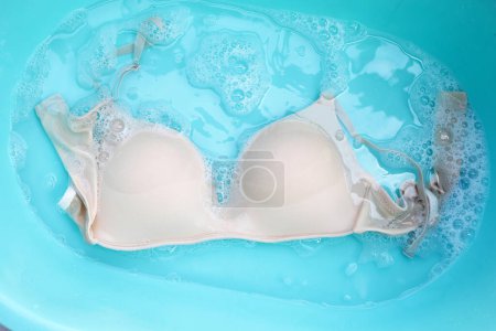 Soutien-gorge Lady trempé dans de l'eau détergent dissous avec bulle de mousse blanche. Concept de blanchisserie