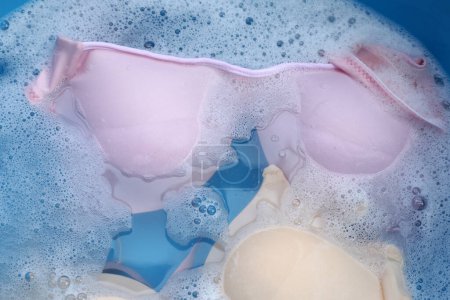 Sujetador de señora empapado en agua detergente disuelto con burbuja de espuma blanca. Concepto de lavandería