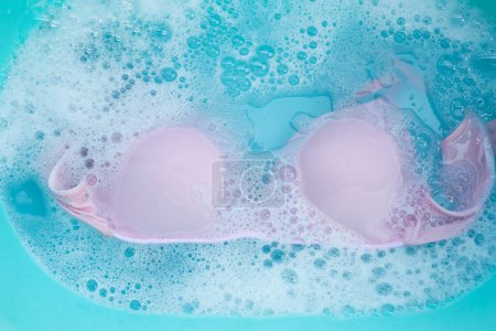 Sujetador de señora empapado en agua detergente disuelto con burbuja de espuma blanca. Concepto de lavandería