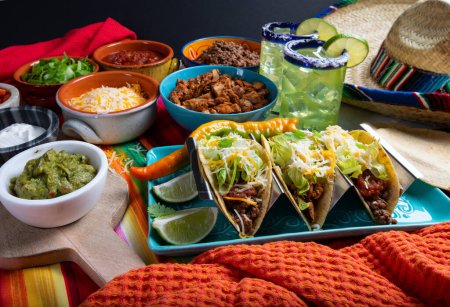 Téléchargez les photos : Tacos avec toutes les garnitures comme le poulet, le boeuf, la crème sure et le fromage sur un fond rustique à servir dans un restaurant avec Sombrero et Margaritas - en image libre de droit