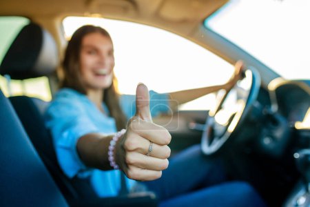 Foto de Hermosa mujer feliz conduciendo su nuevo coche y mostrando los pulgares hacia arriba gesto al atardecer . - Imagen libre de derechos