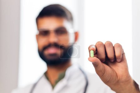 Foto de Doctor wearing uniform and showing a pill in hand blurred person. - Imagen libre de derechos