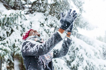 Foto de African american man in a snowy winter woodland with snowflakes falling from spruce and fir forest. - Imagen libre de derechos