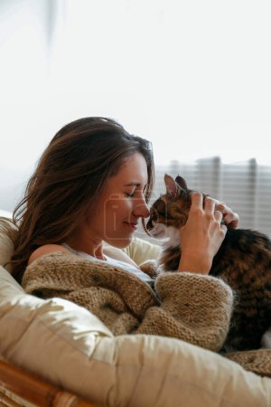 Portrait of young woman holding cute norwegian cat with green eyes. Female hugging her cute long hair kitty. Background, copy space, close up.