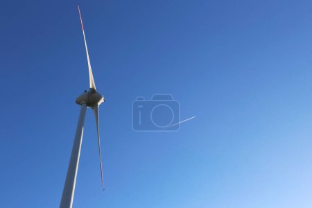 Photo for Close up shot of the wind turbine blades over the clear blue sky background with the airplane contrail. - Royalty Free Image