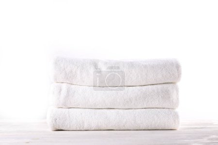 Stack of neatly folded towels on a rustic wooden table, waiting to be used. Showcase of a cozy bathroom or spa setting against a plain white background. Studio shot, close up, copy space.