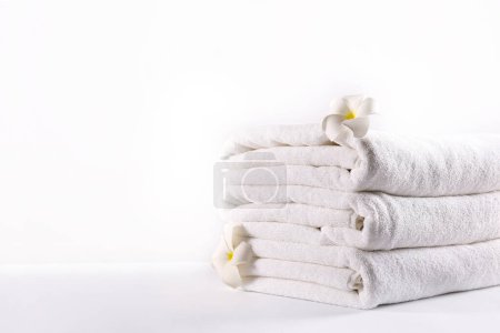 Stack of neatly folded towels on a rustic wooden table, waiting to be used. Showcase of a cozy bathroom or spa setting against a plain white background. Studio shot, close up, copy space.