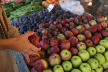 Cropped shot of a young woman picking fresh apples on farmers market. Plant based diet concept. Conscious shopping for organic local produce fruits. Close up, copy space, background.
