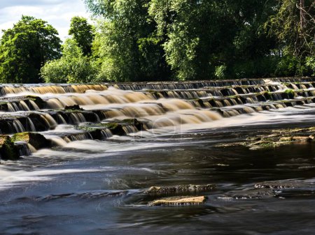 Photo for A beautiful weir across the river Wharfe at Burley-in-wharfedale in England. The weir is in 4 steps and the flow is slow as the river isn't running fast. It is a lovely, sunny Summers day. - Royalty Free Image