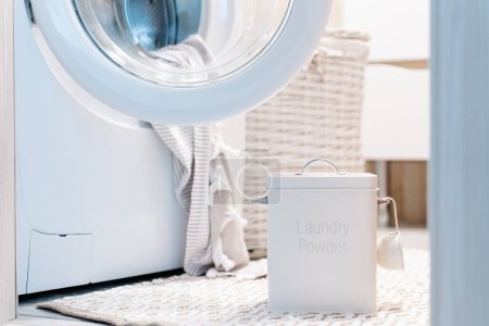 Washing powder in tin container nearby washing machine, peshtemal towel in washing machine. High quality photo