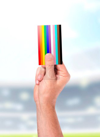 Téléchargez les photos : Un arbitre sportif masculin ou une main d'arbitre tenant en l'air une carte couleur LGBTQ sur fond de stade sportif - en image libre de droit