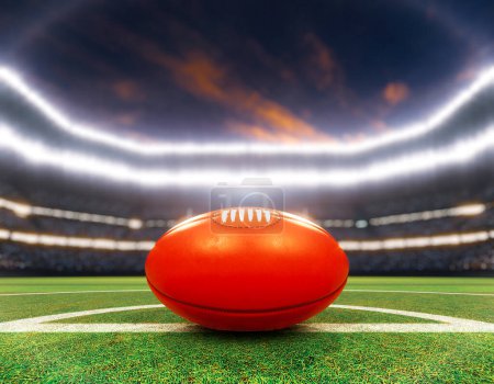 Téléchargez les photos : Une aussie rouge règle la balle sur la ligne centrale d'un stade avec des poteaux sur un terrain d'herbe verte marquée la nuit sous des projecteurs éclairés - rendu 3D - en image libre de droit