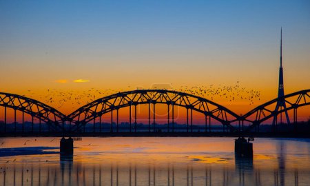 A beautiful sunrise scenery with iron bridge over the frozen river Daugava in Latvian capital city Riga. Winter landscape of Northern Europe.