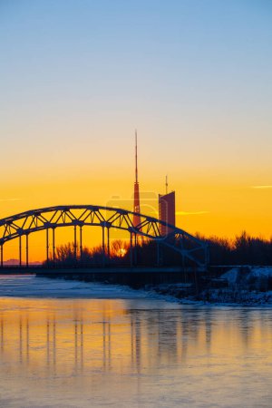 Téléchargez les photos : Un magnifique lever de soleil avec pont en fer sur la rivière gelée Daugava dans la capitale lettone Riga. Paysage hivernal du nord de l'Europe. - en image libre de droit