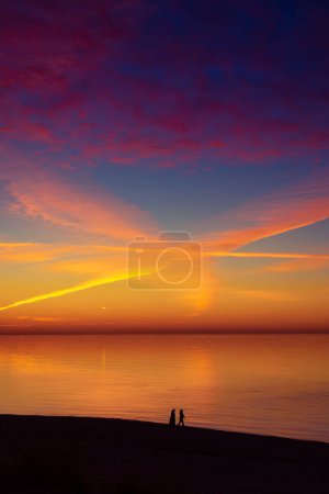 Téléchargez les photos : Un beau paysage de coucher de soleil de personnes profitant de la soirée à la plage de la mer Baltique. Silhouettes humaines face à la mer en Europe du Nord. - en image libre de droit