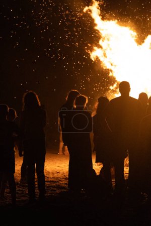 Téléchargez les photos : Les gens regardent le feu brûler sur la plage de la mer Baltique pendant le festival du feu en été. Lumineux, feu chaud. - en image libre de droit