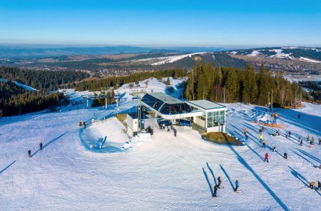 Ski slope, chairlift, skiers and snowboarders in Bialka Tatrzanska ski resort in Poland on Jankulakowski Wierch Mountain in winter. Aerial view in sunset light