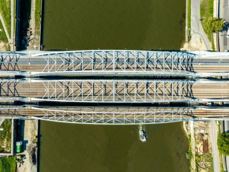 Photo for Triple tied-arc railroad bridge with four tracks, footbridge for pedestrians and bicycle lane over Vistula river in Krakow, Poland. Aerial view from above - Royalty Free Image