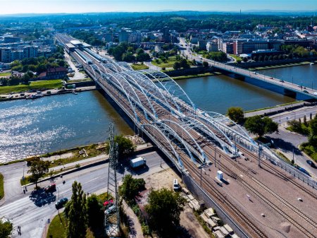 Neue dreibogige Eisenbahnbrücke mit vier Gleisen, Fußgängerbrücke und Radweg über die Weichsel in Krakau, Polen. Weite Sicht auf den neuen Bahnhof Krakau Zablocie. Luftaufnahme