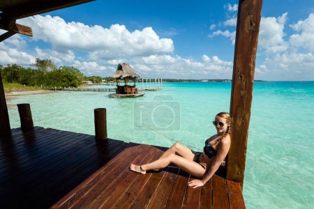 Téléchargez les photos : Beautiful landscape with young woman relaxing on a wooden pier in Laguna Bacalar in Mexico during kayak trip. - en image libre de droit