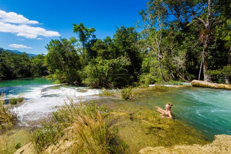 Photo for Young pretty woman relaxing by the water in Roberto Barrios cascadas park, Palenque in Mexico. Vivid landscape photo with lush green and crystal water during sunny day. - Royalty Free Image